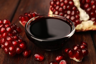 Photo of Glass bowl of tasty pomegranate sauce and fresh ripe fruit on wooden table, closeup