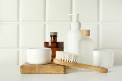 Photo of Bath accessories. Personal care products and wooden brush on white table near tiled wall