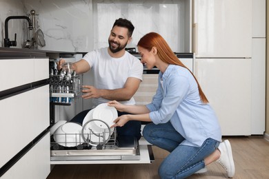 Happy couple loading dishwasher with plates in kitchen