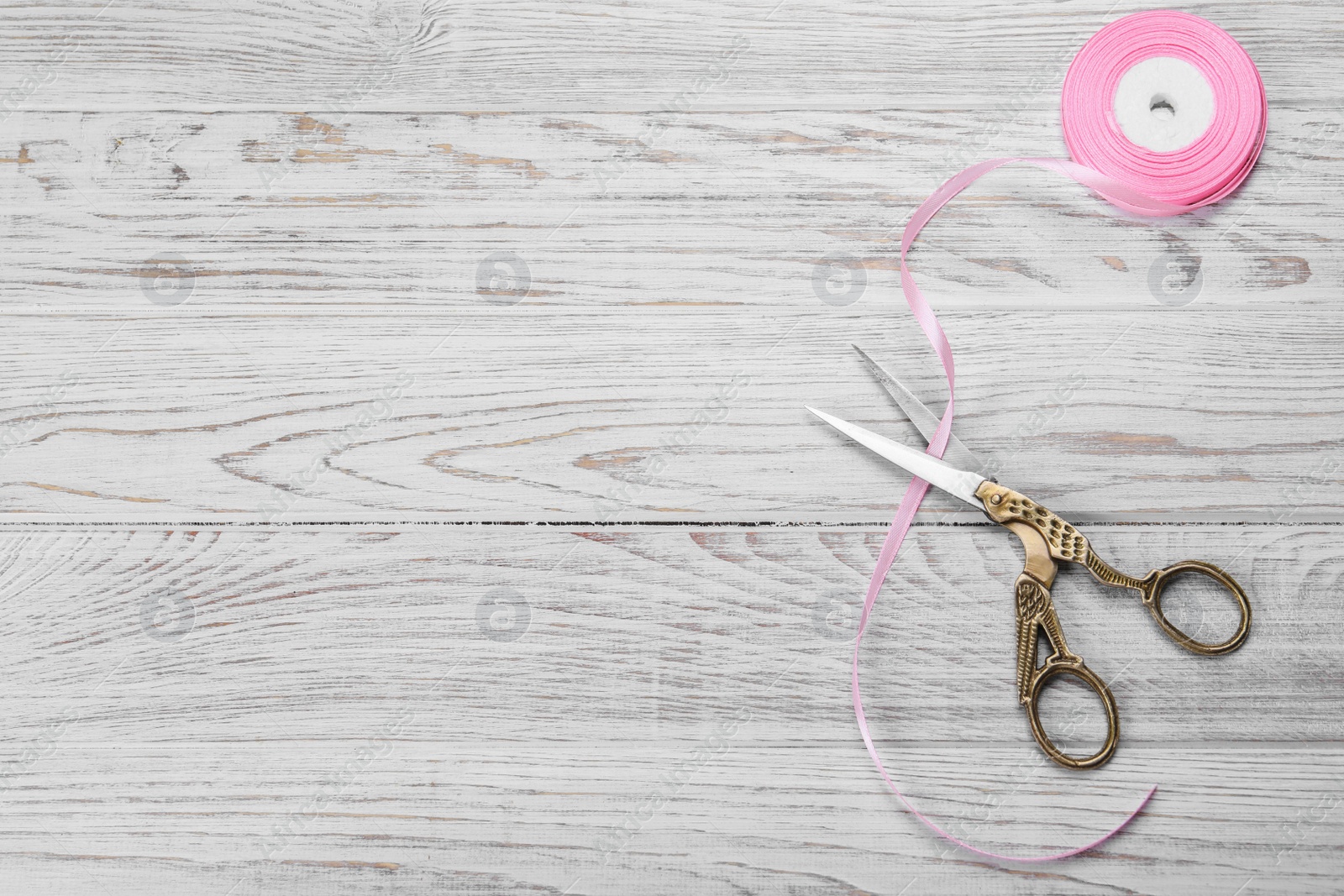 Photo of Scissors and pink ribbon on white wooden table, flat lay. Space for text