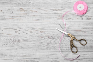 Scissors and pink ribbon on white wooden table, flat lay. Space for text