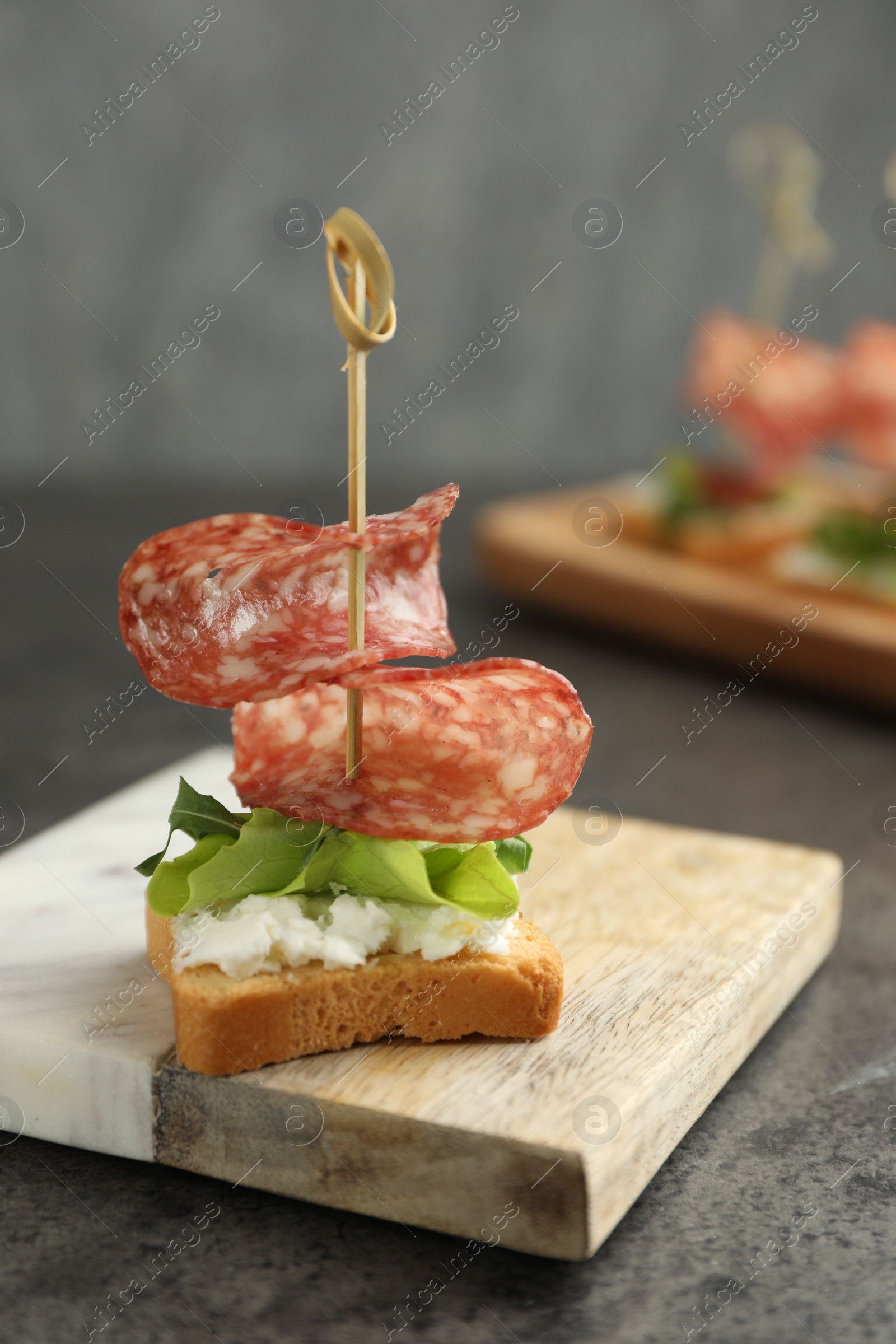 Photo of Tasty canape with salami, greens and cream cheese on grey table