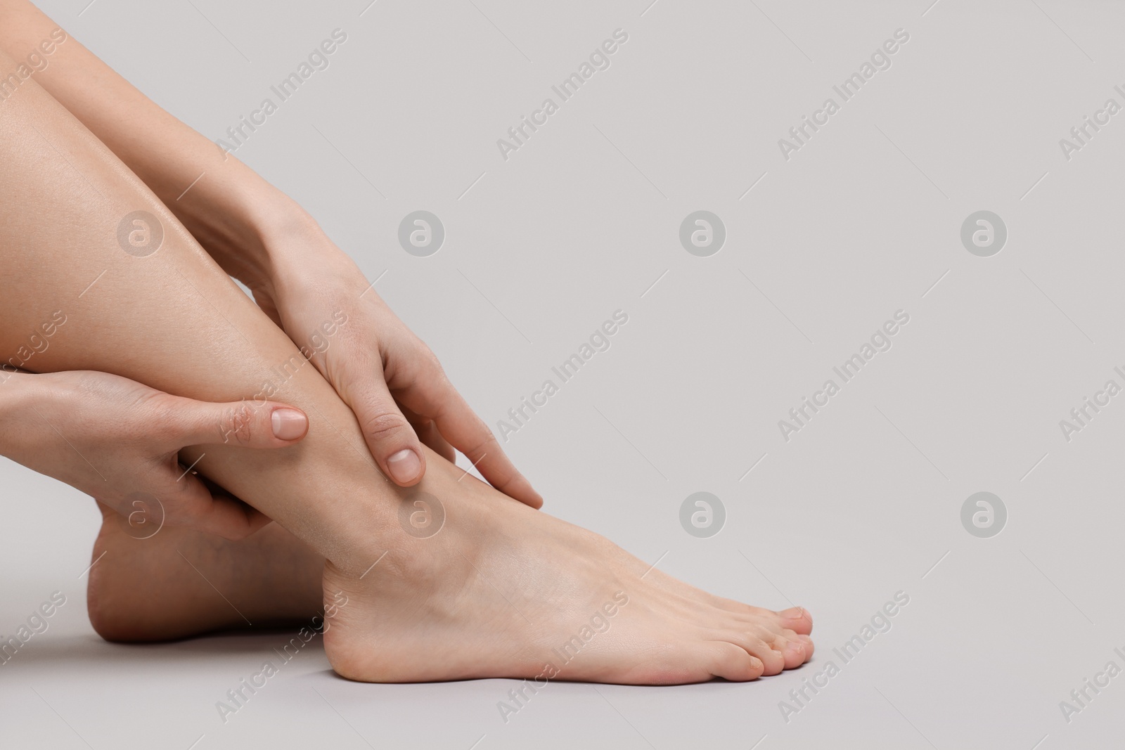 Photo of Woman suffering from leg pain on grey background, closeup. Space for text