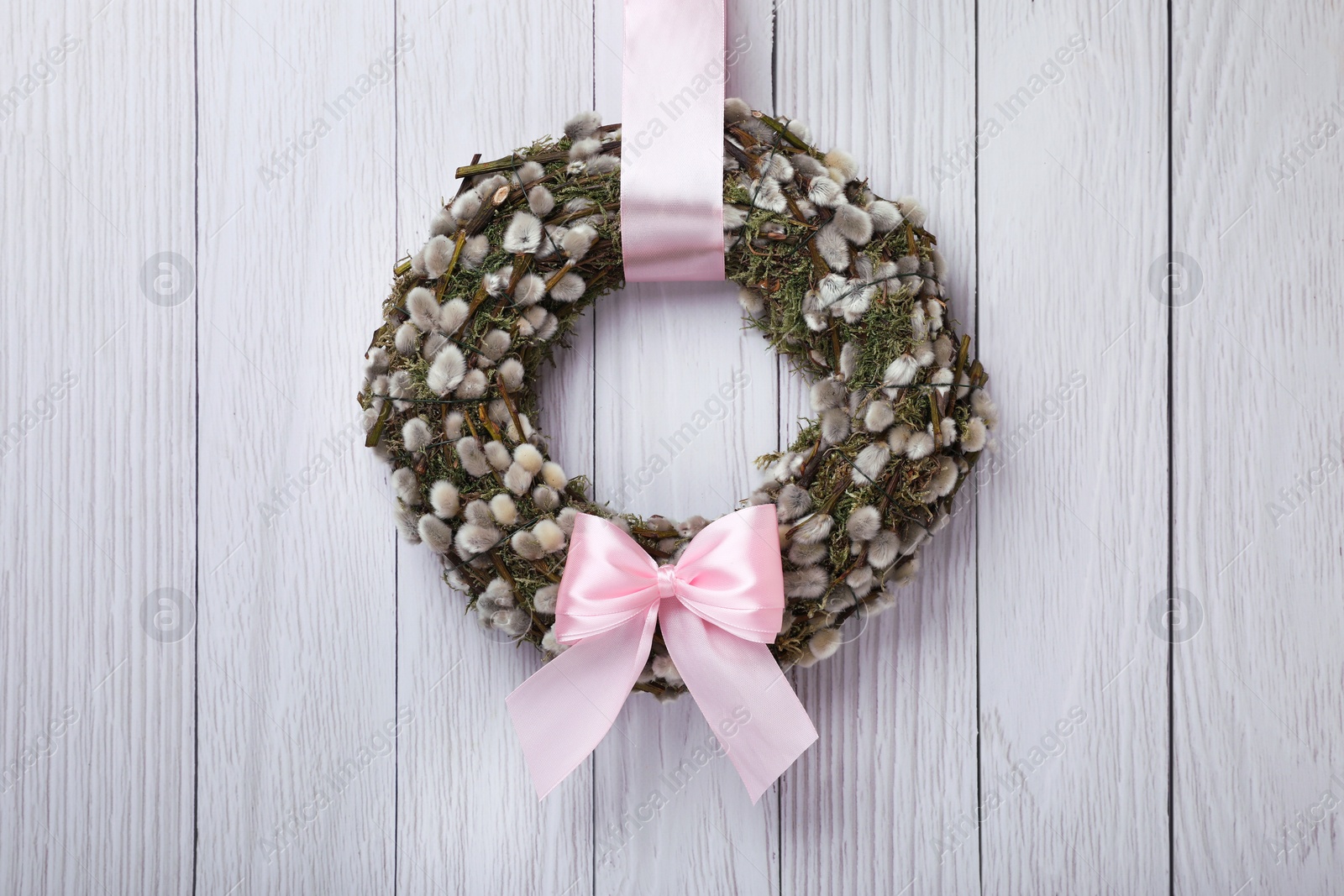 Photo of Wreath made of beautiful willow branches and pink bow hanging on white wooden background