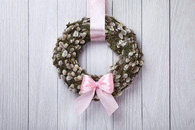 Wreath made of beautiful willow branches and pink bow hanging on white wooden background