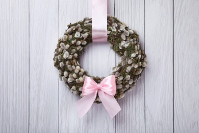 Photo of Wreath made of beautiful willow branches and pink bow hanging on white wooden background