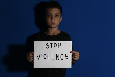 Photo of Abused little boy with sign STOP VIOLENCE near blue wall