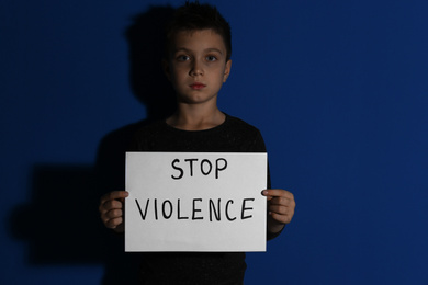 Abused little boy with sign STOP VIOLENCE near blue wall