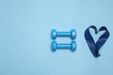 Photo of Two dumbbells and fitness elastic band in shape of heart on light blue background, flat lay. Space for text