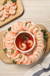 Photo of Tasty boiled shrimps with cocktail sauce, chili and parsley on light wooden table, flat lay