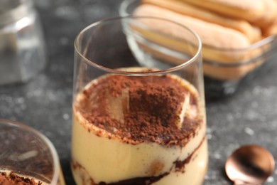 Photo of Delicious tiramisu in glass on grey table, closeup