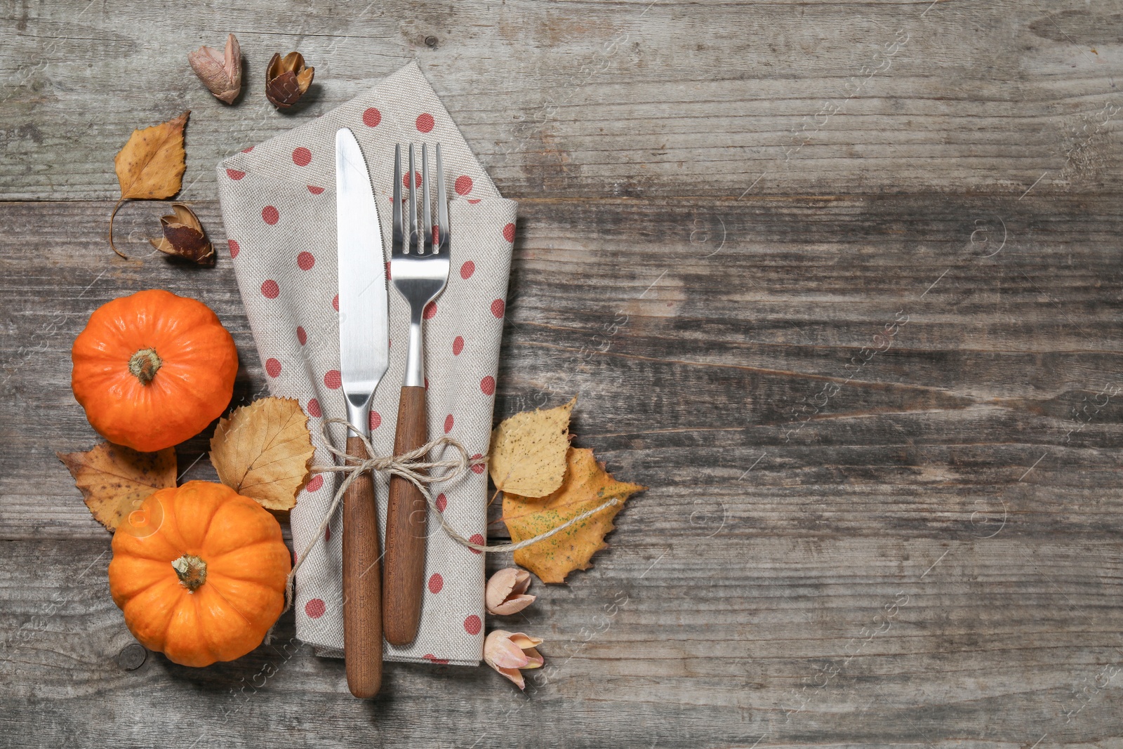 Photo of Thanksgiving day table setting. Cutlery, napkin and autumn decoration on wooden background, flat lay with space for text