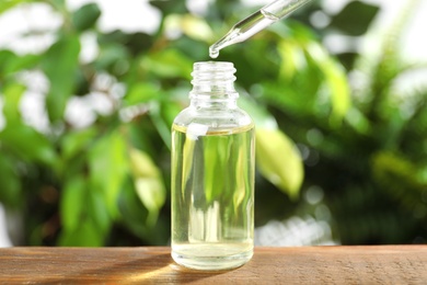 Dropper with essential oil over bottle on wooden table against blurred background