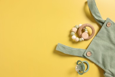 Photo of Baby accessories. Rattle, pacifier and overall on yellow background, flat lay. Space for text