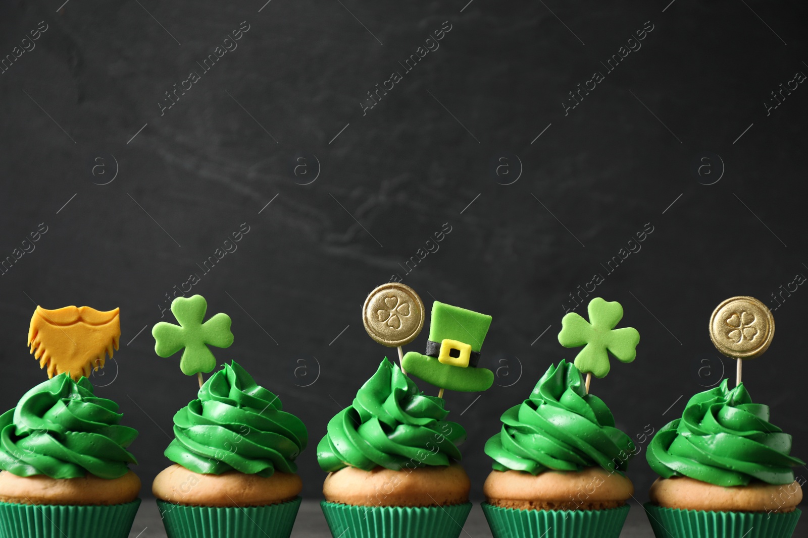 Photo of Delicious decorated cupcakes on dark grey background, space for text. St. Patrick's Day celebration