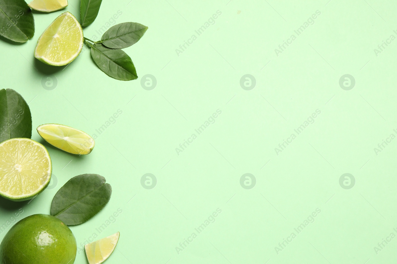 Photo of Whole and cut fresh ripe limes with leaves on light green background, flat lay