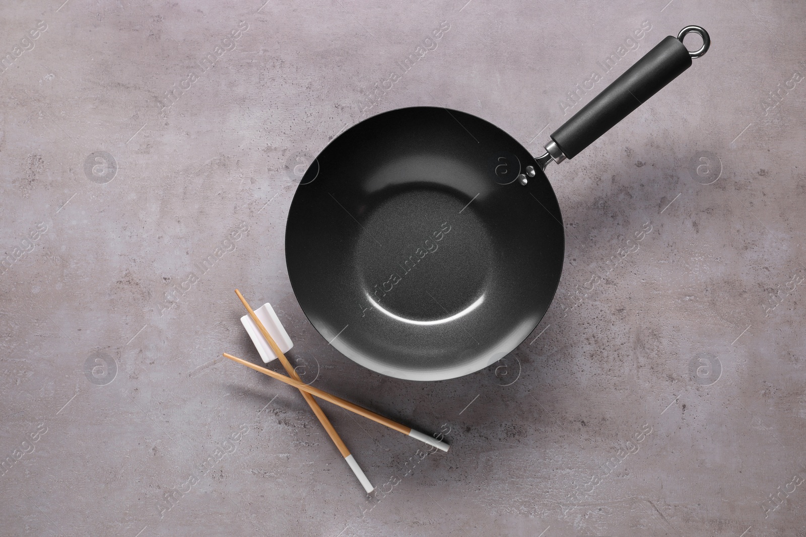 Photo of Empty iron wok and chopsticks on grey table, flat lay