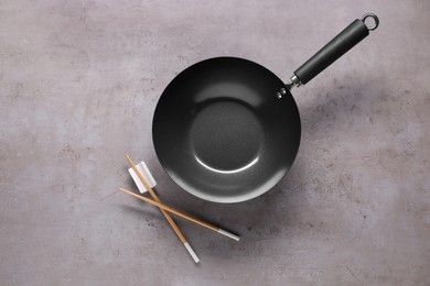 Empty iron wok and chopsticks on grey table, flat lay