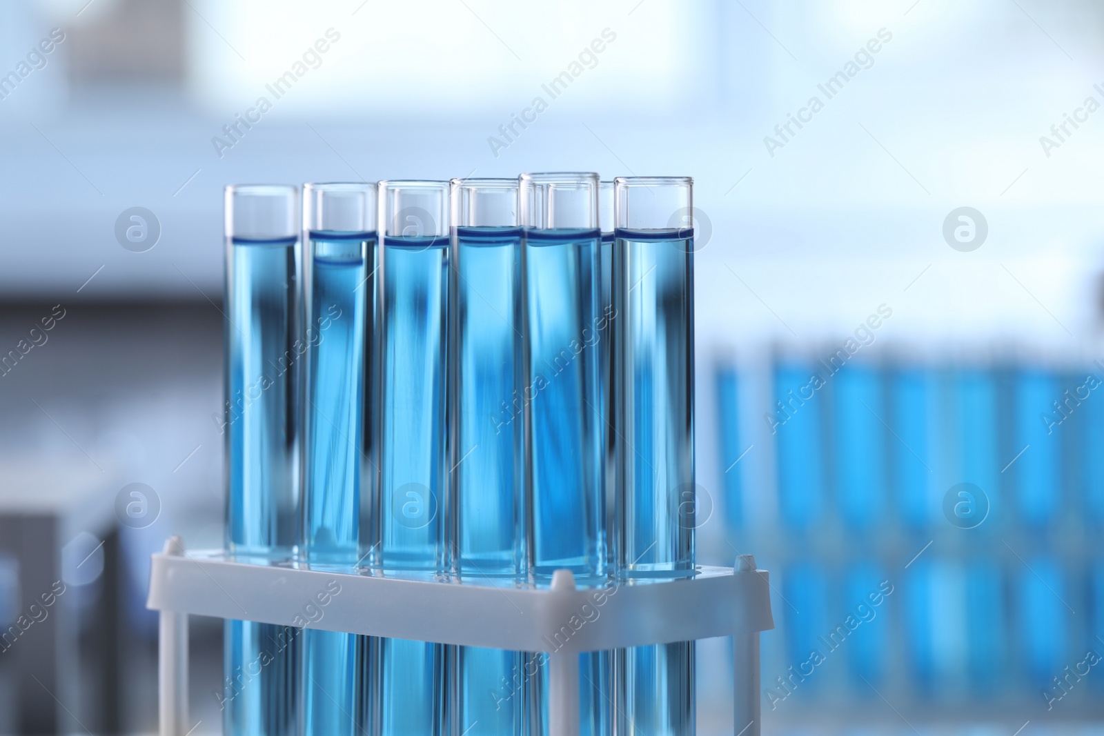 Photo of Test tubes with light blue liquid on blurred background, closeup