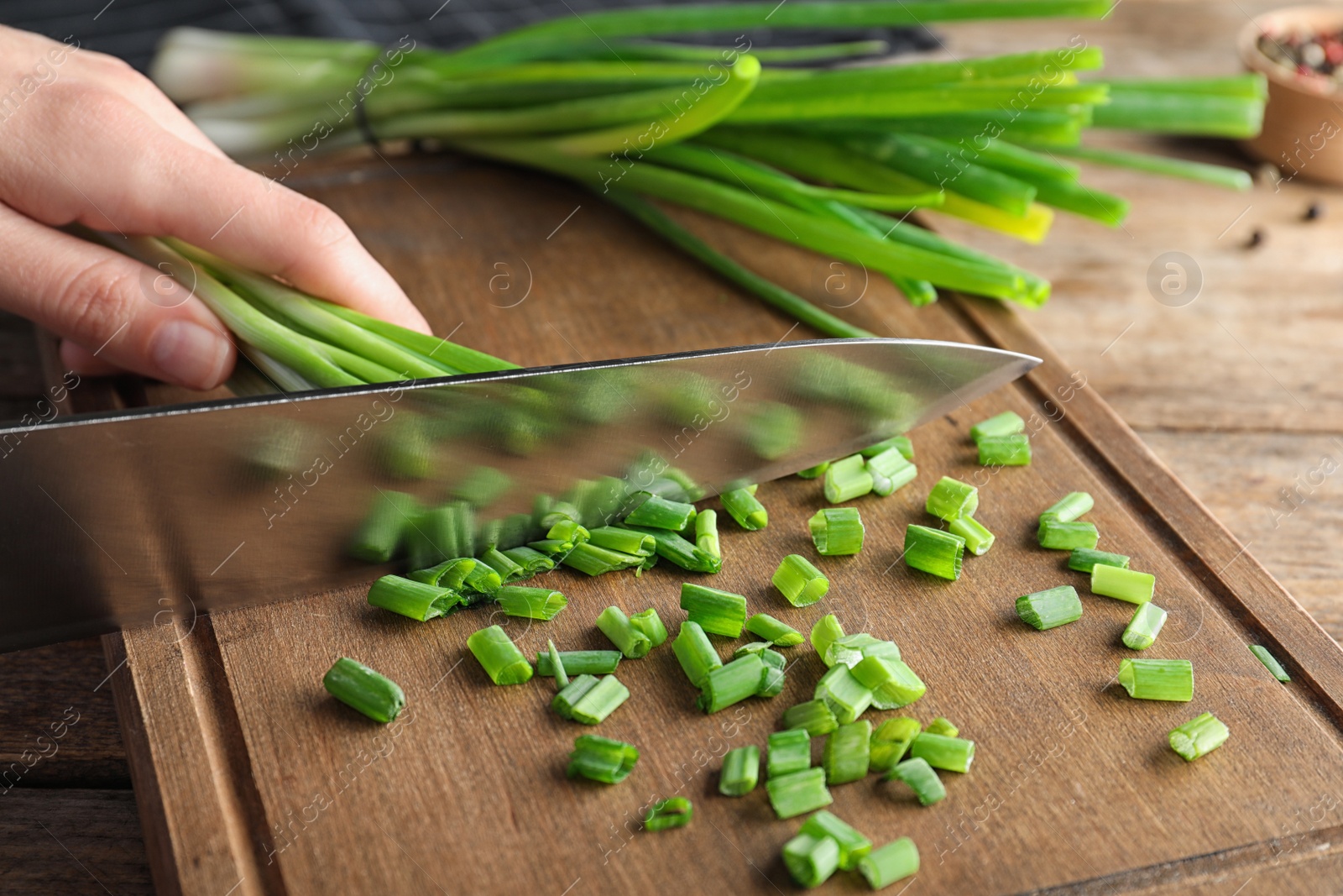 Photo of Woman cutting fresh green onion on wooden board at table, closeup