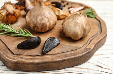 Photo of Board with tasty black garlic on white wooden table