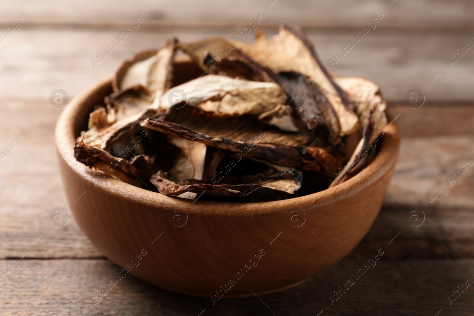 Photo of Bowl of dried mushrooms on wooden background, closeup