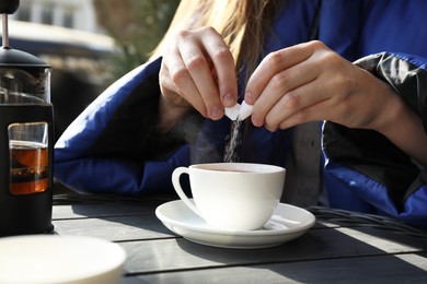 Photo of Woman adding sugar into cup of tea at black wooden table in outdoor cafe, closeup