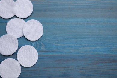 Many clean cotton pads on light blue wooden table, flat lay. Space for text