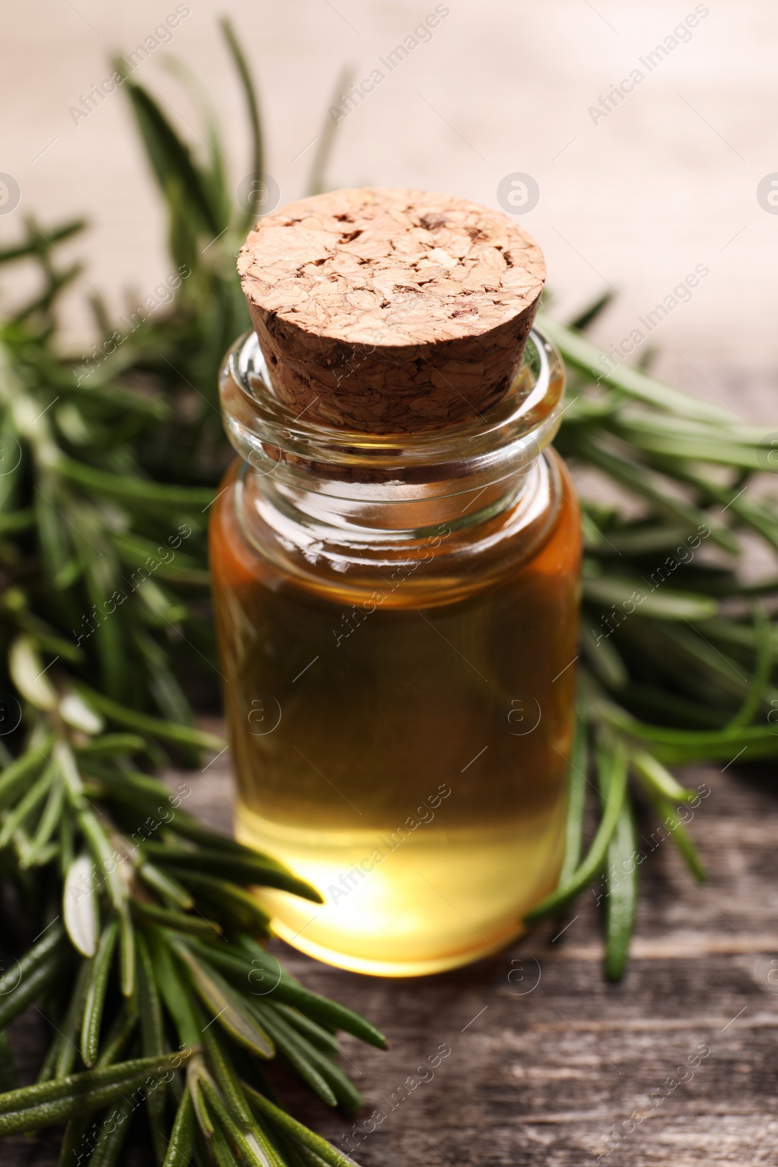 Photo of Bottle of essential oil and fresh rosemary on wooden table, closeup