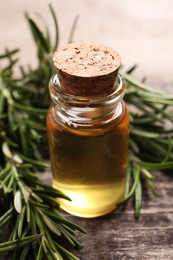 Bottle of essential oil and fresh rosemary on wooden table, closeup