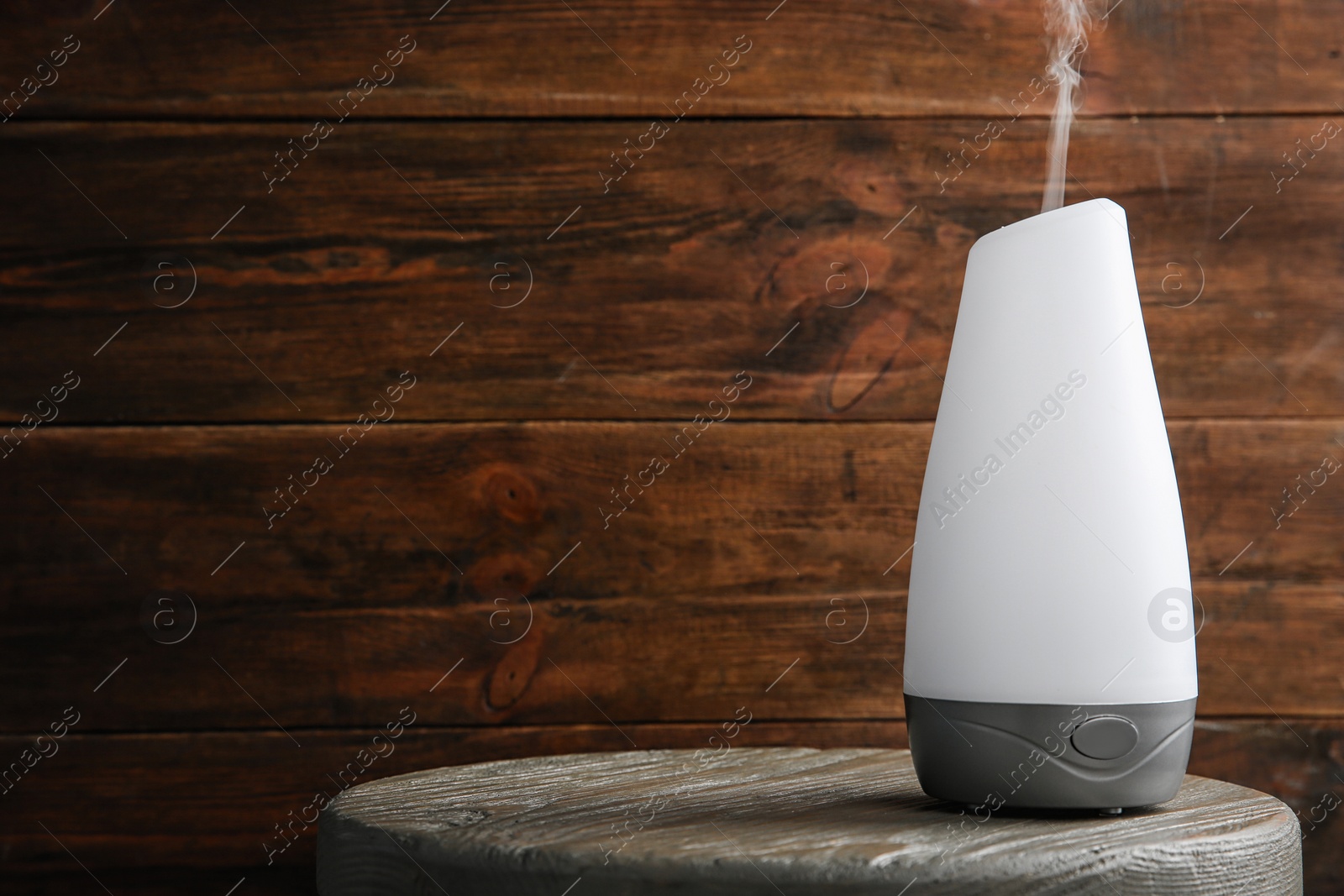 Photo of Modern essential oil diffuser on wooden table against brown background. Space for text