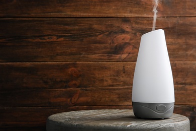 Photo of Modern essential oil diffuser on wooden table against brown background. Space for text