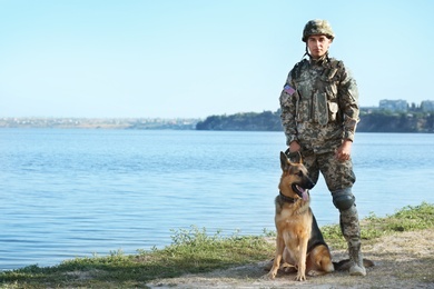 Photo of Man in military uniform with German shepherd dog near river, space for text