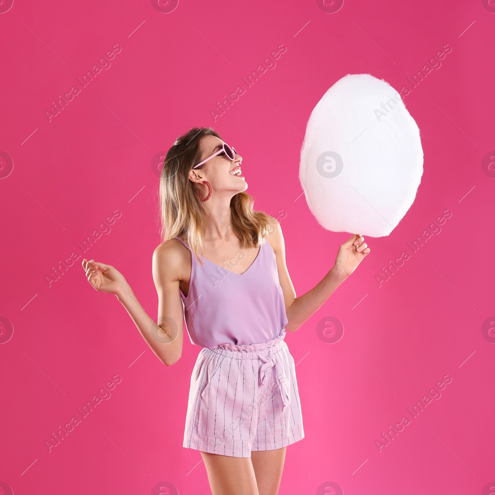 Photo of Happy young woman with cotton candy on pink background