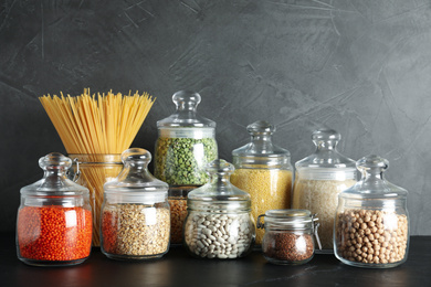 Glass jars with different types of groats and pasta on black table