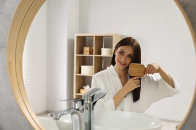 Photo of Beautiful woman brushing her hair near mirror in bathroom, space for text