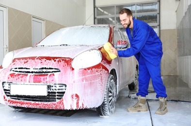 Photo of Worker cleaning automobile with sponge at professional car wash