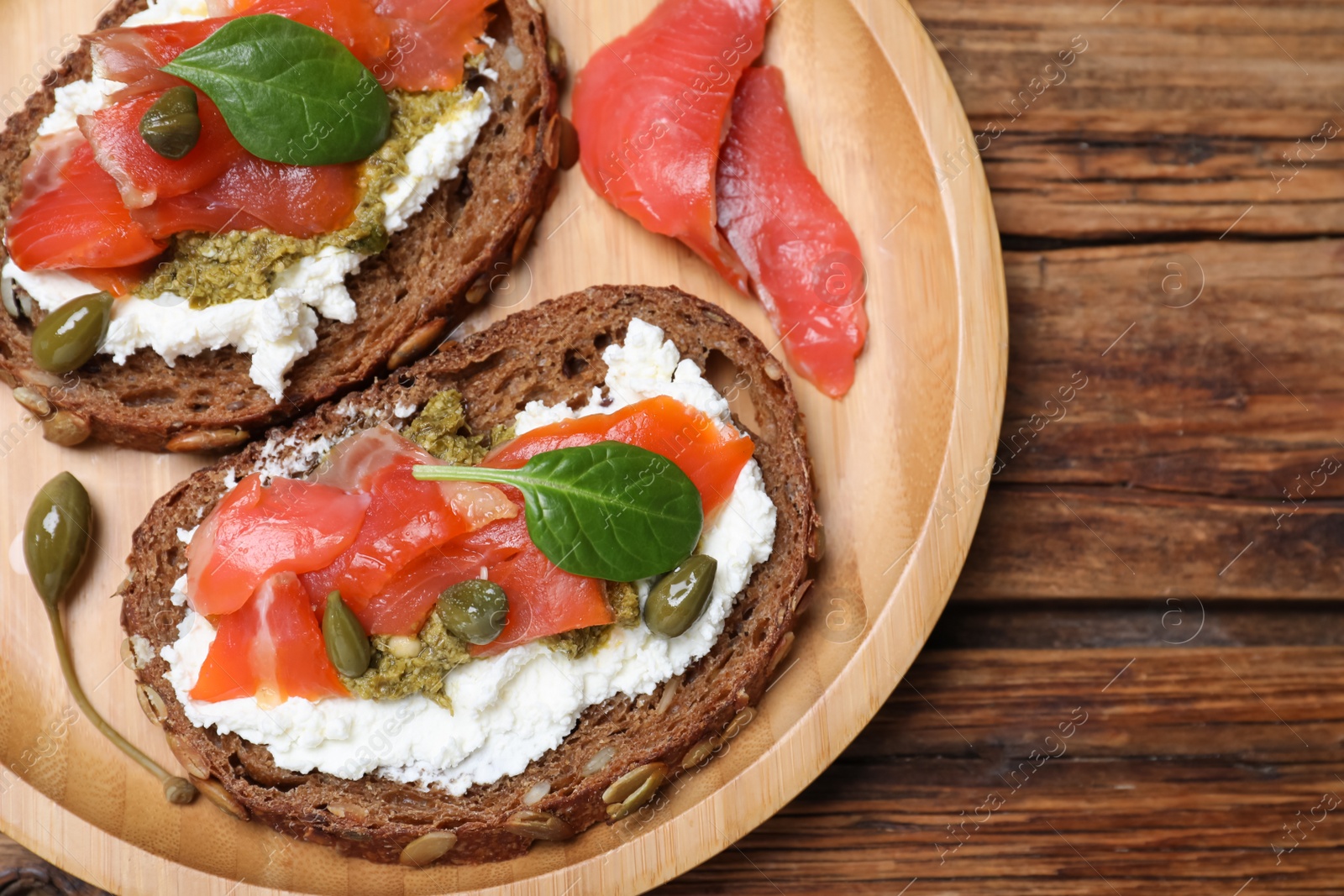 Photo of Delicious sandwiches with cream cheese, salmon, capers and pesto on wooden table, top view