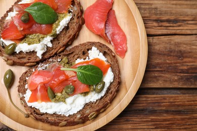 Delicious sandwiches with cream cheese, salmon, capers and pesto on wooden table, top view