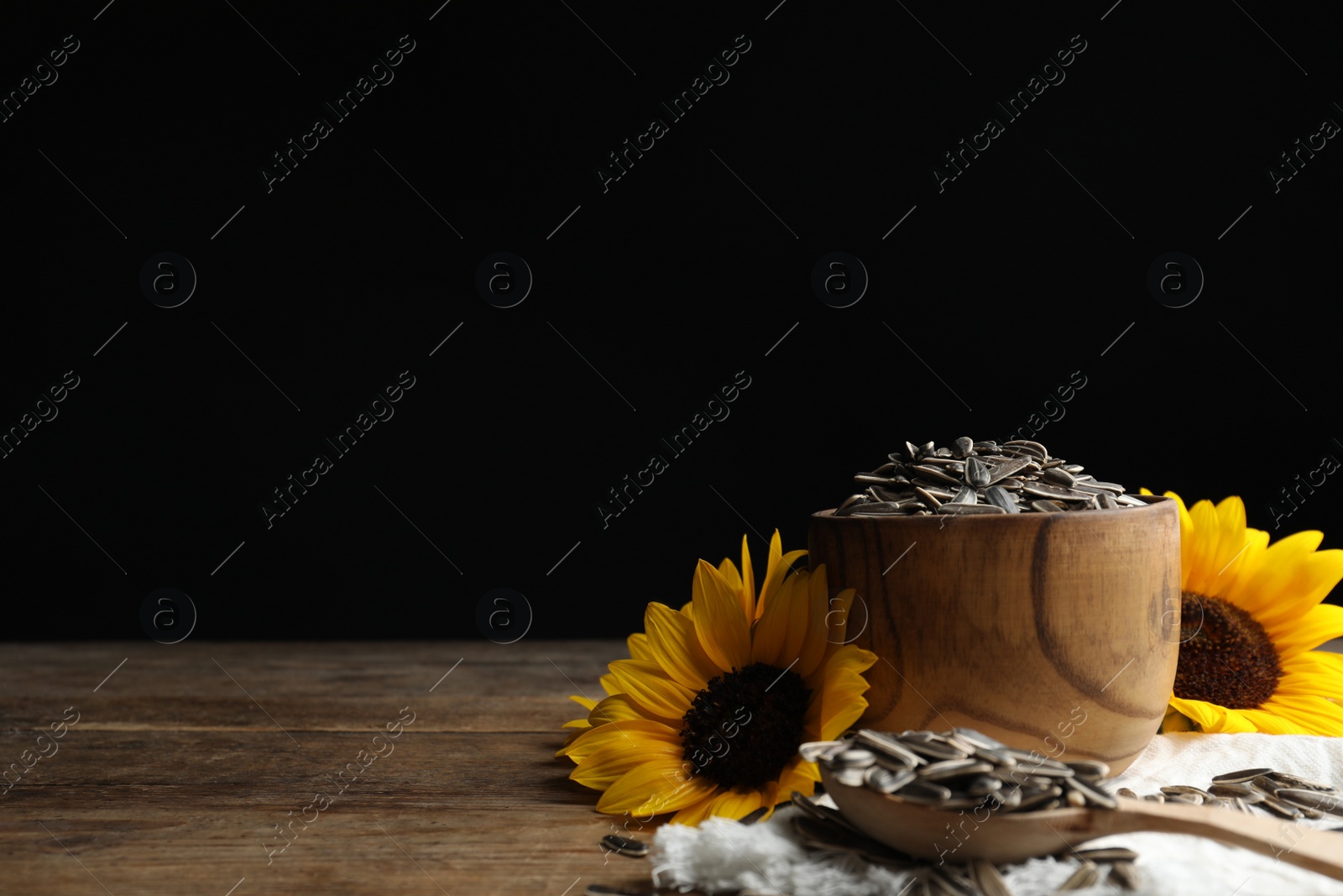 Photo of Organic sunflower seeds and flowers on wooden table. Space for text