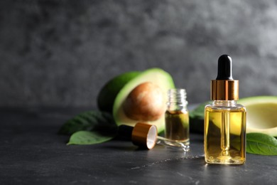 Bottle of essential oil and fresh avocado on black table, space for text