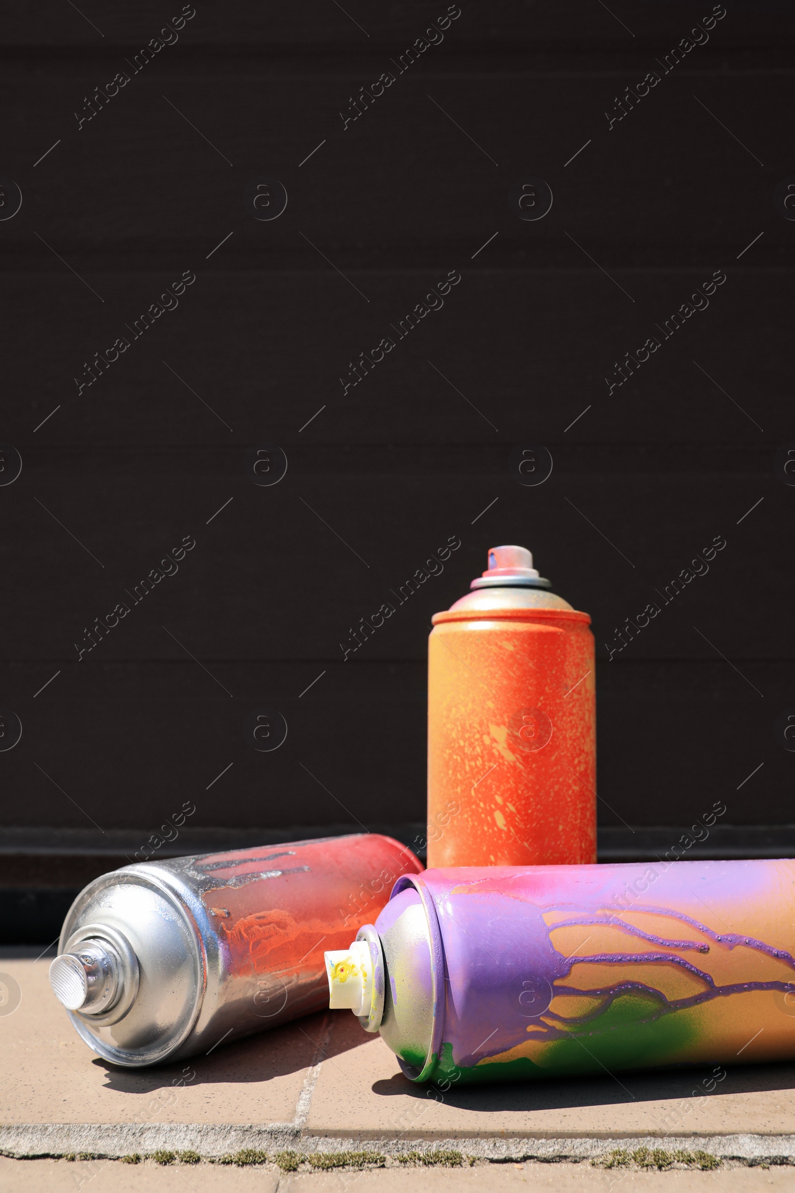 Photo of Used cans of spray paint on tile floor near black wall outdoors, space for text. Graffiti supplies