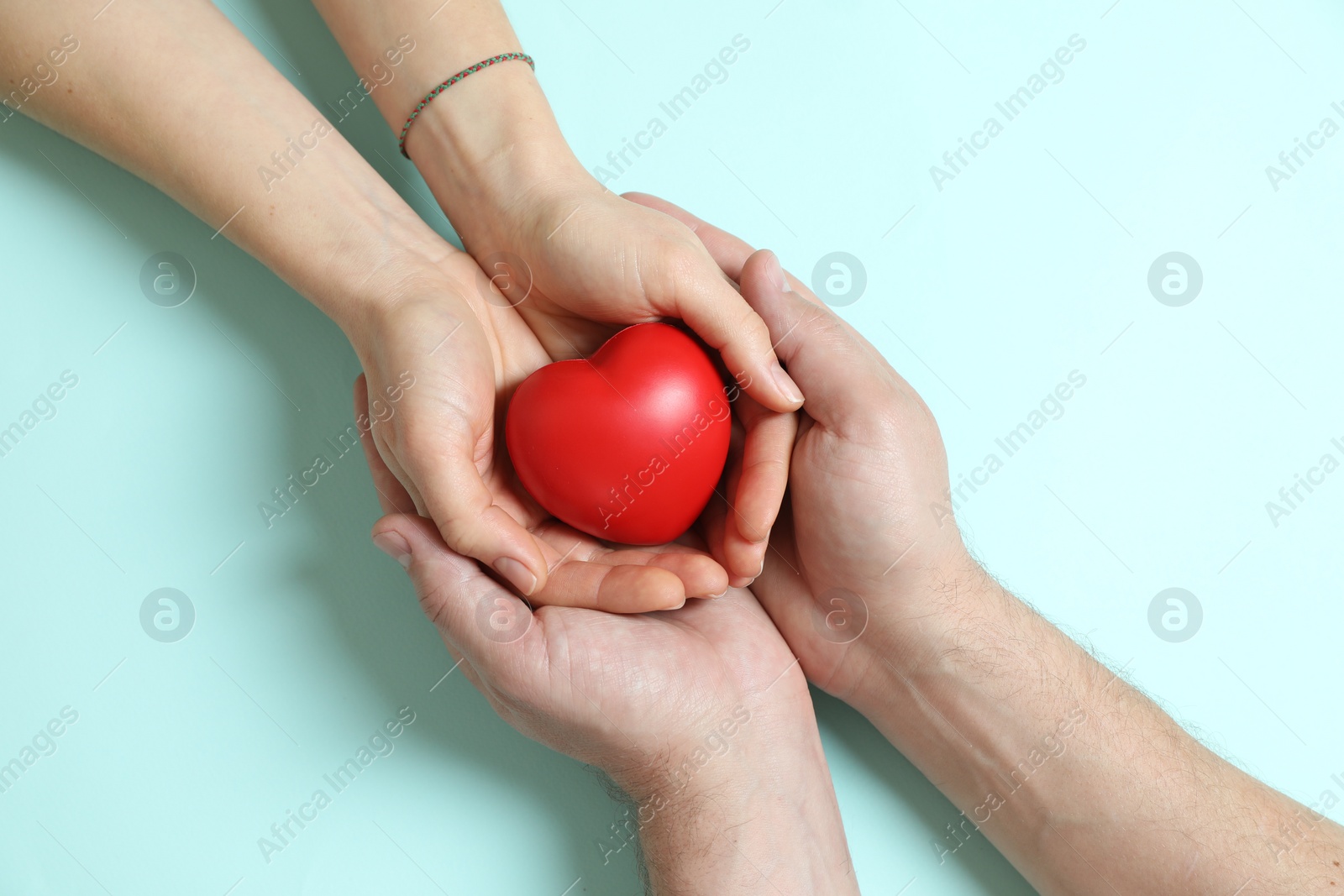 Photo of Couple holding red decorative heart on light blue background, top view