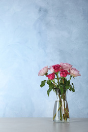 Beautiful roses in glass vase on light grey table. Space for text