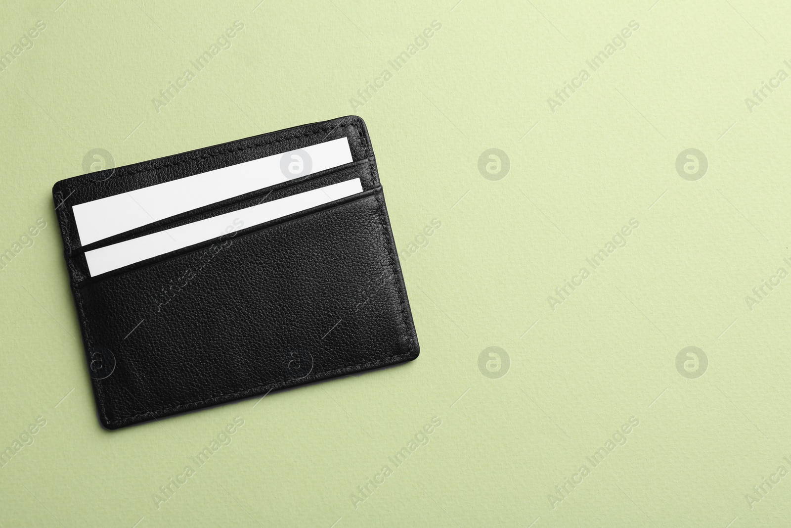 Photo of Leather business card holder with blank cards on light green background, top view. Space for text