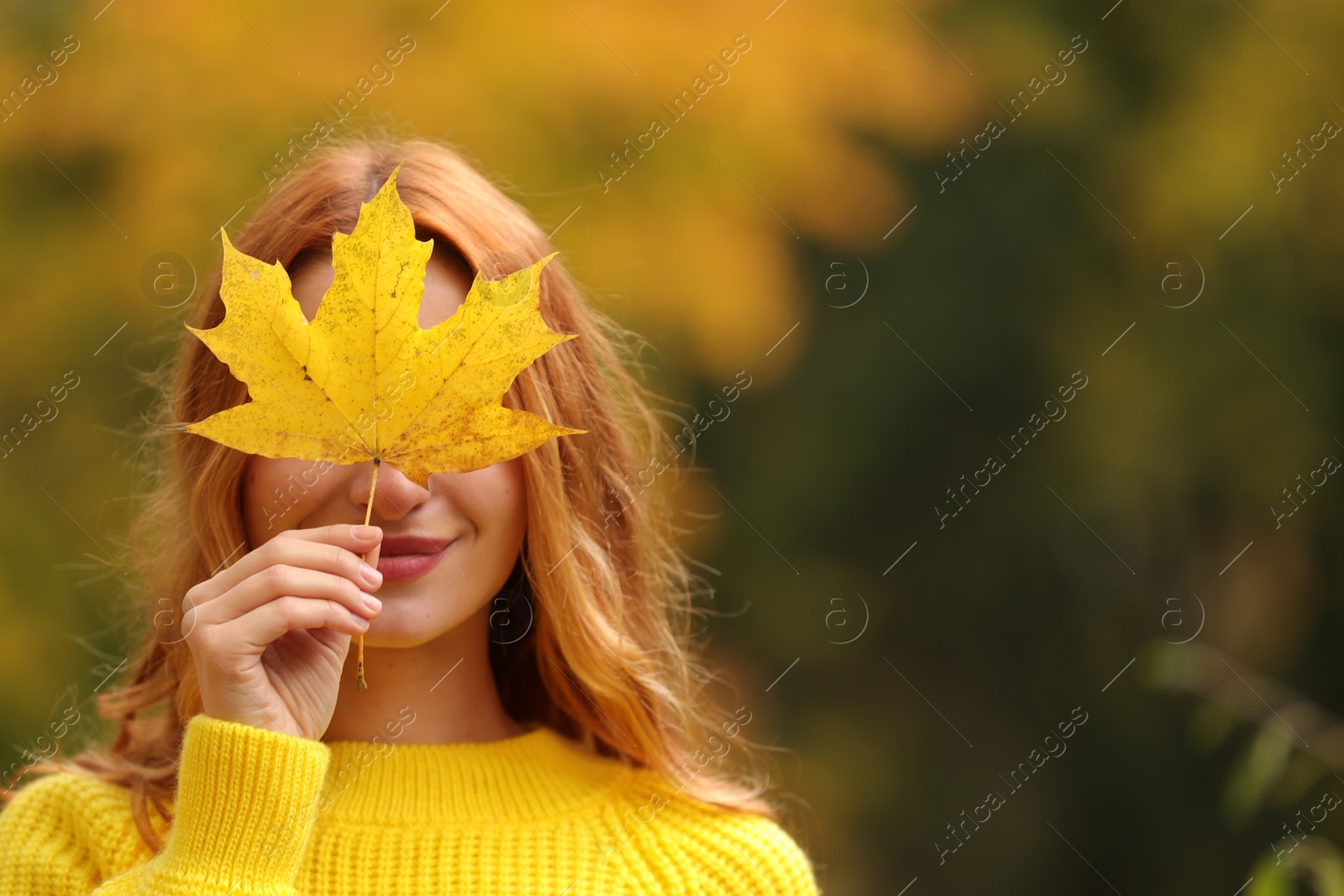 Photo of Woman covering face with autumn leaf outdoors. Space for text