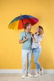 Couple with rainbow umbrella near color wall