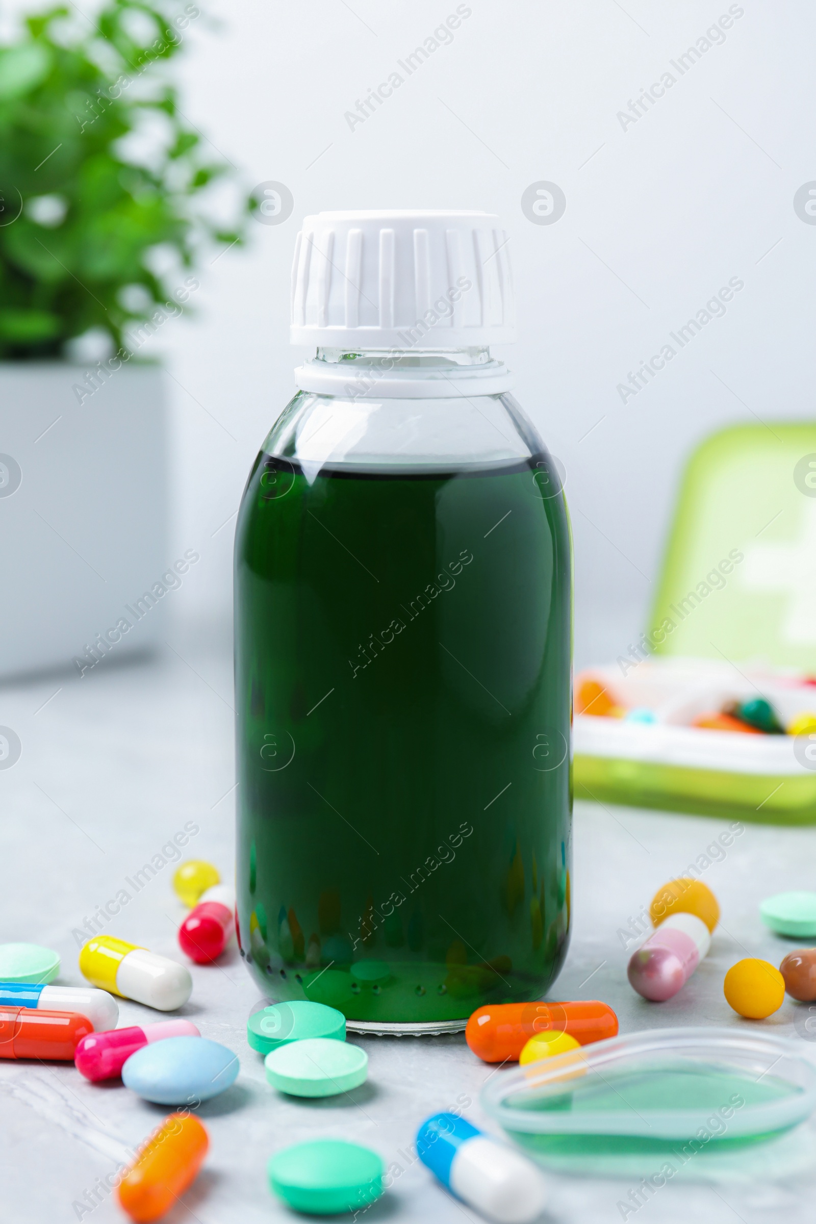 Photo of Bottle of syrup, dosing spoon and pills on white table. Cold medicine