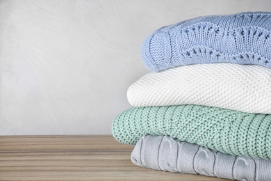 Stack of folded warm sweaters on wooden table. Space for text