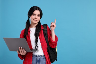Photo of Smiling student with laptop pointing at something on light blue background. Space for text